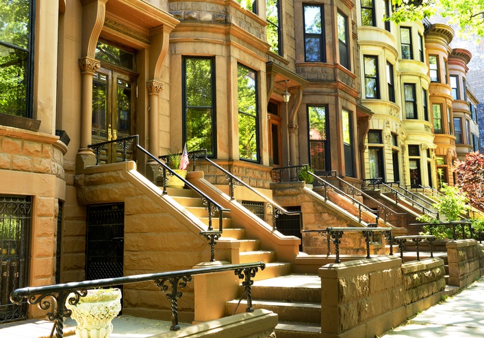 Exterior of several differently sand-coloured brownstone houses in a row on a New York street