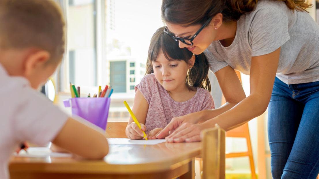 Children drawing with smiling preschool teacher