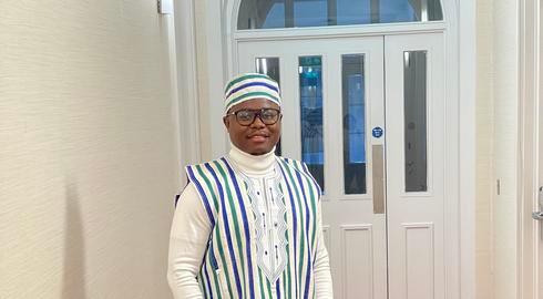 Emmanuel Sandy smiles while stood wearing the colours of Sierra Leone on a red carpet in a corridor with cream wallpaper and a white door.