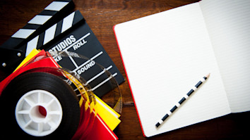 Open notebook and pencil for a creative screen writer with film reel, more notebooks and a clapperboard