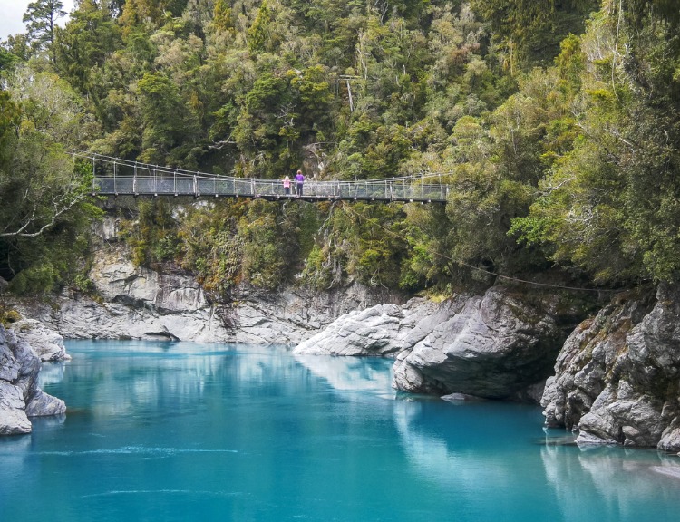 tourists admire the beautiful hokitika gorge from the swing bridge