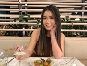Anna smiles while holding chopsticks at a restaurant table containing a drink and plate of food