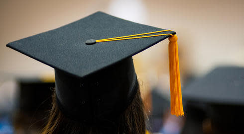A person with long hair wears a graduation cap at a ceremony with other new graduates