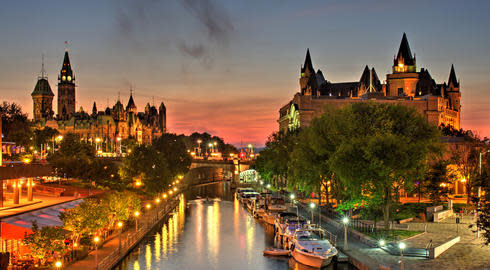 A red sky at dusk over Ottawa, as seen from the lamp-lit, boat-lined Rideau Canal. To the left is Parliament Hill and to the right is Château Laurier hotel.