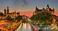 A red sky at dusk over Ottawa, as seen from the lamp-lit, boat-lined Rideau Canal. To the left is Parliament Hill and to the right is Château Laurier hotel.