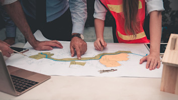 People around a table looking at a design drawing, with a laptop nearby