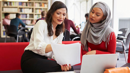 University Student Working In Library With Tutor