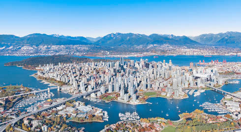 Aerial shot of Downtown Vancouver with mountains in the background and skyscrapers and bridges in the foreground.