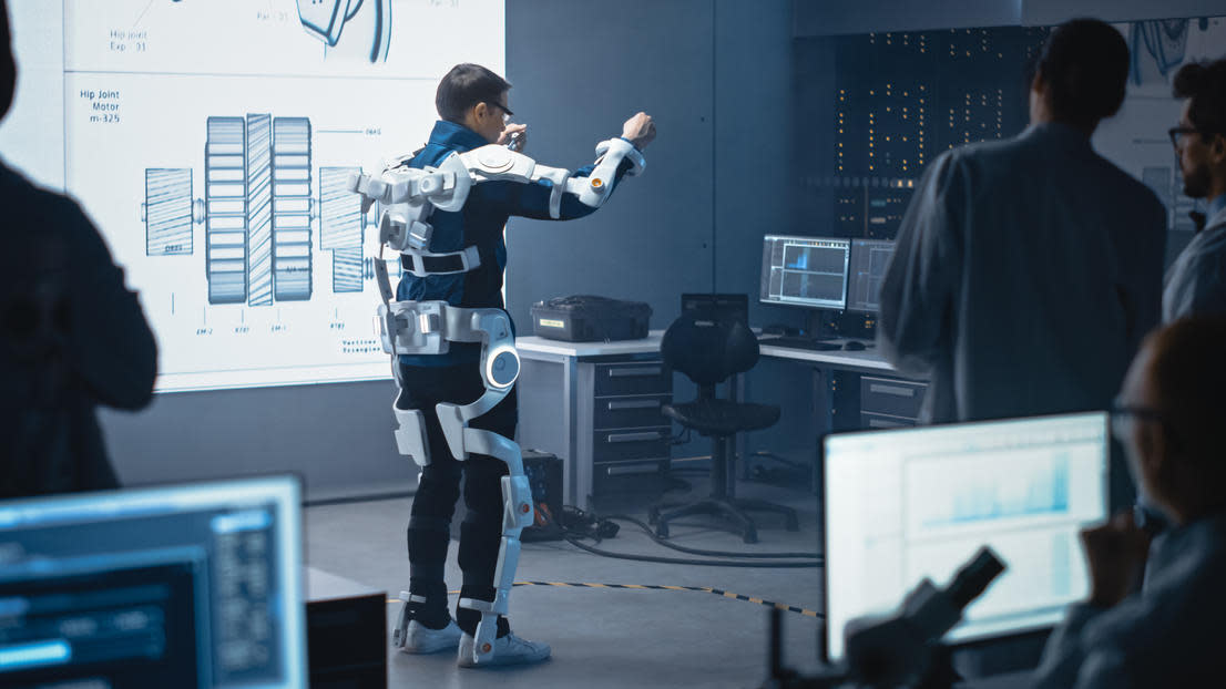 Engineers and scientists look at robotics exoskeleton prototype on human tester