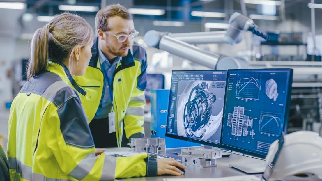 Mechanical Engineer Holds Component while Chief Engineer Works on Computer