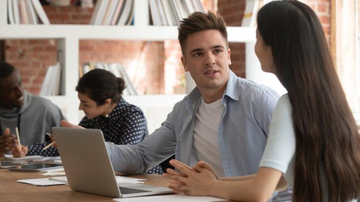 University mates sit at shared desk work at laptop discuss college assignment