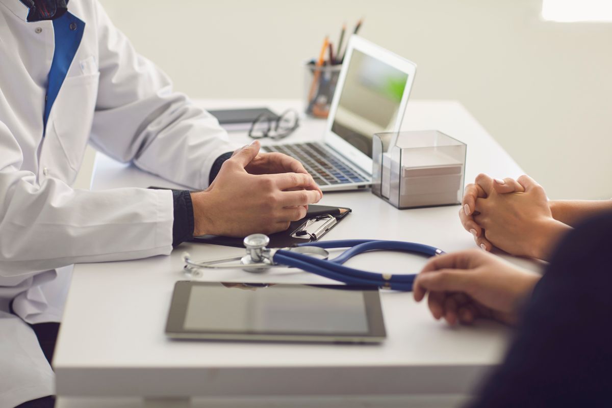 Dua orang pasien sedang berkonsultasi dengan seorang dokter dalam ruang praktik dokter