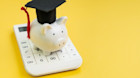 Piggybank with a grad cap sat on a white calculator 