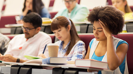 Group of students sitting and writing in a lecture hall with coffee