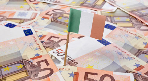 A small Irish flag stands above a pile of 50 Euro notes