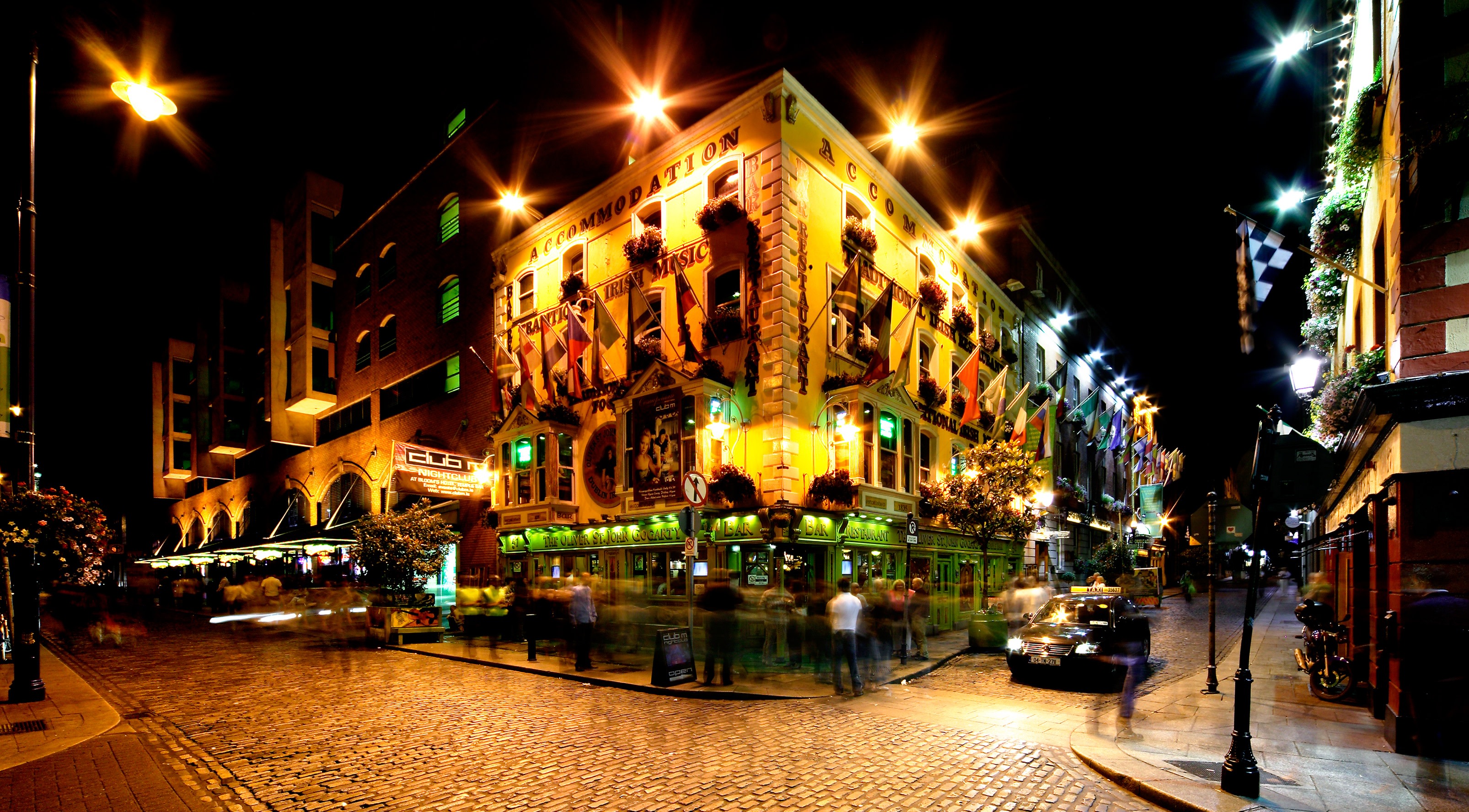 Temple Bar in Dublin at night. A number of people stand outside a well-lit pub on the corner of two pedestrianised roads.