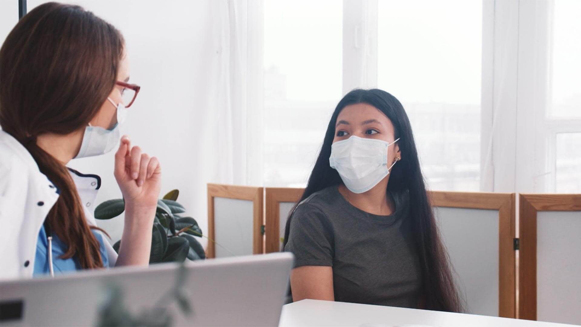 woman talking to her doctor, both wearing masks