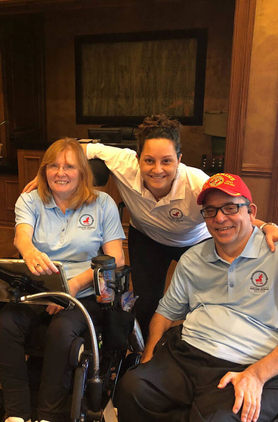 3 people smiling for a photo, two are in wheelchairs.