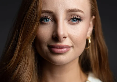 Businesswoman with long red hair and bright blue eyes is giving a subtle smile