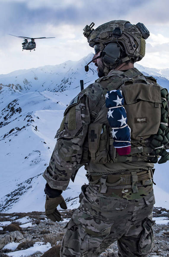 Solider standing in the mountains with a helicopter in the background