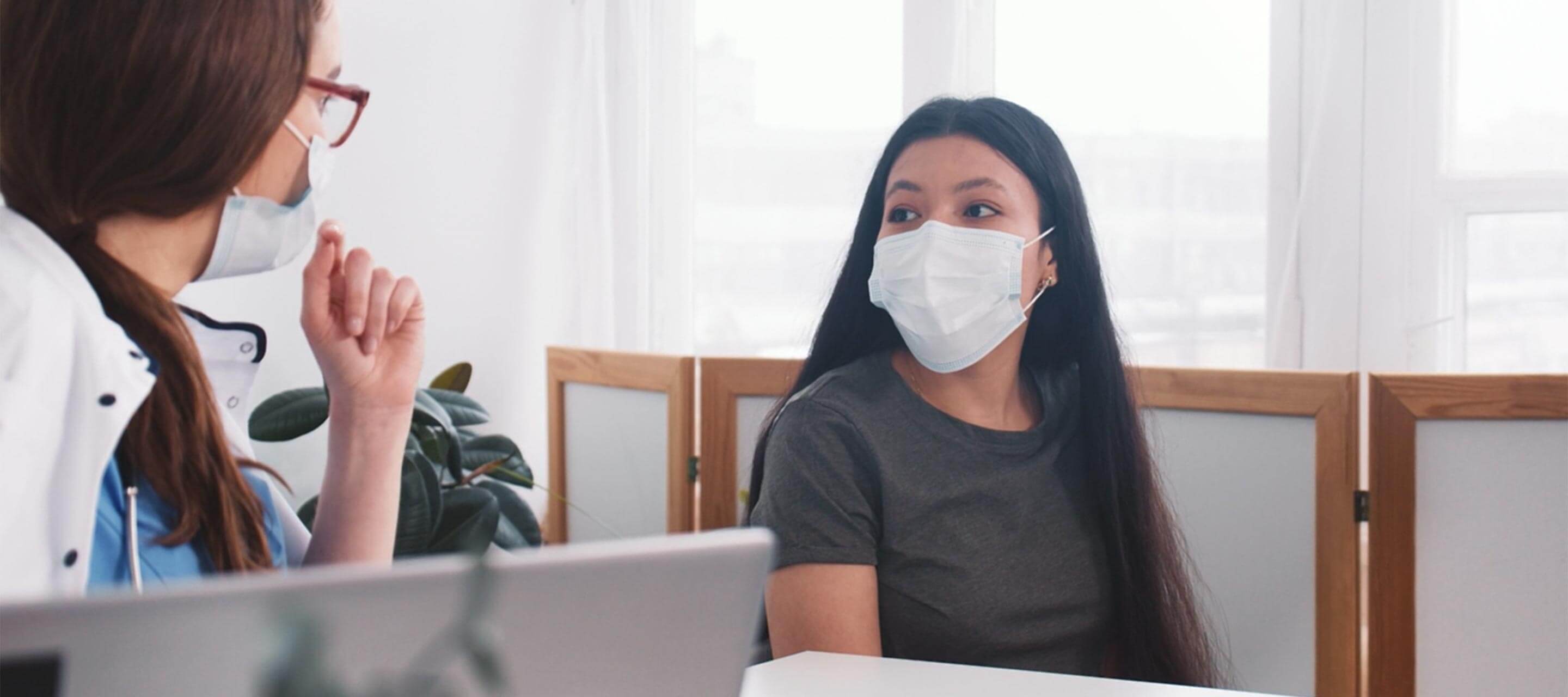 woman talking to her doctor, both wearing masks