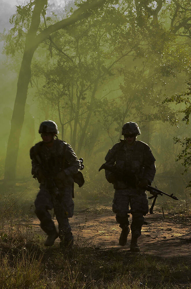 two soldier silhouettes walking through green forest 