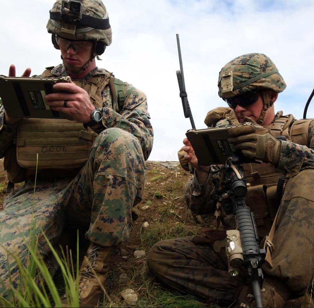 2 soldiers sitting on the field looking at their tablets
