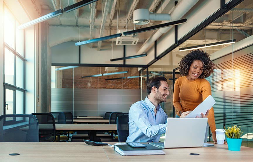 a man and woman in the office looking at paperwork together 