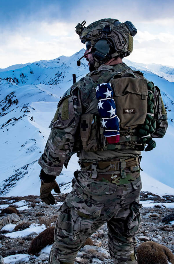 Military man standing on a snowy mountain with helicopter overhead