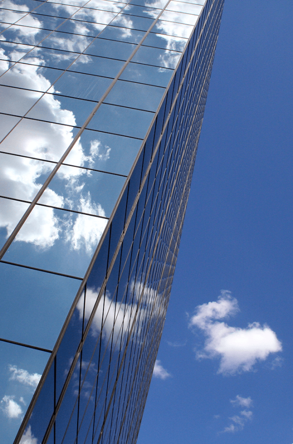 corner of glass building with windows reflecting blue sky with clouds 