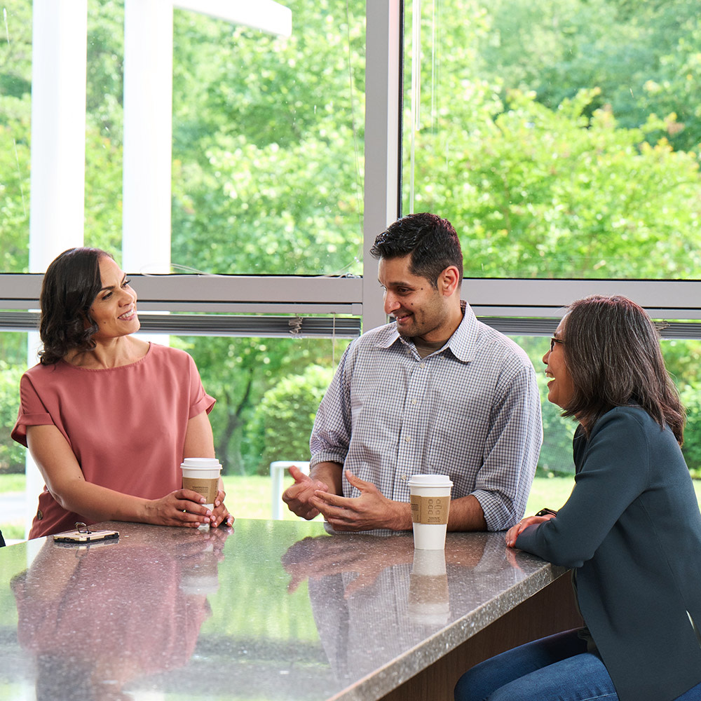 GDIT employees gathered together around a table drinking coffee and talking