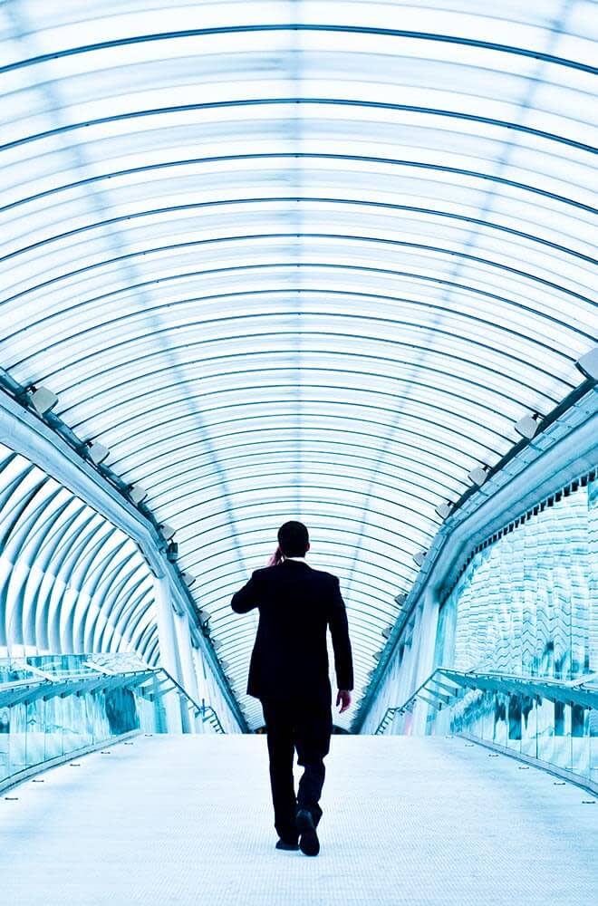 person walking through glass tunnel wearing suit, talking on phone. 