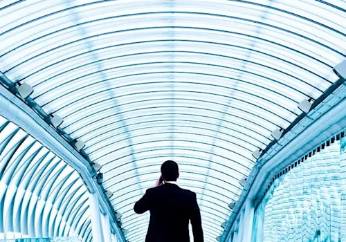 person walking through glass tunnel wearing suit, talking on phone.