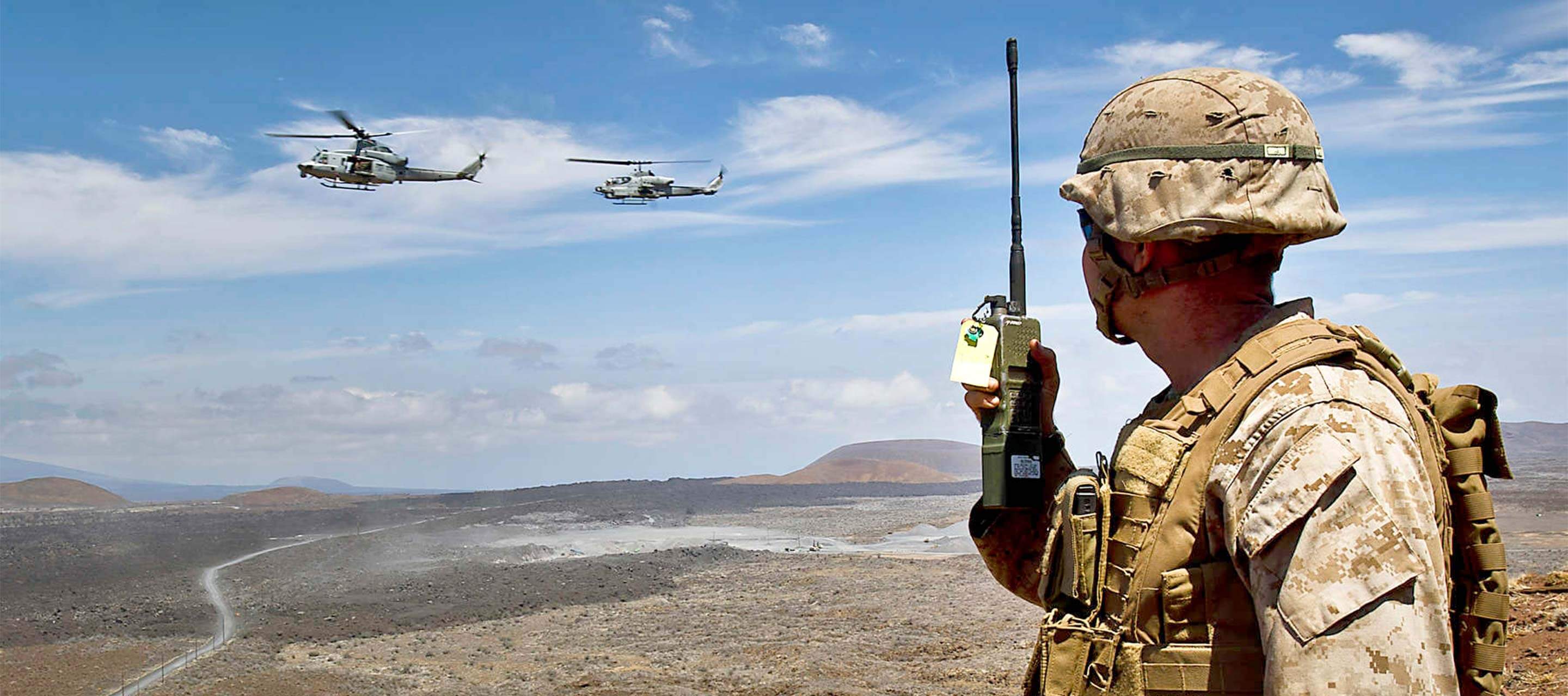 soldier on his walkie talkie looking at helicopters flying by