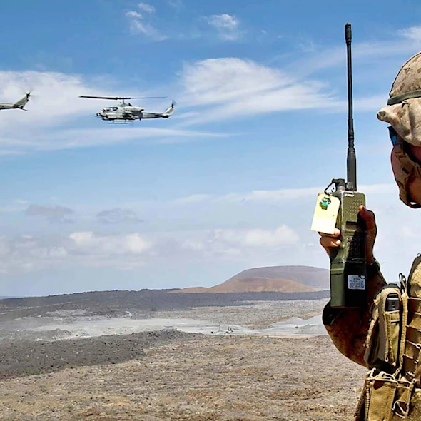 soldier on his walkie talkie looking at helicopters flying by