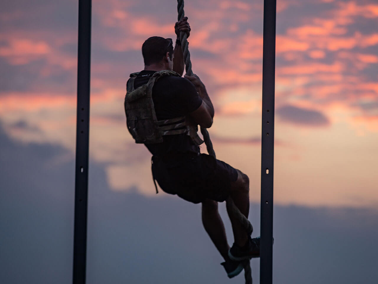 person climbing rope, sunset in the background