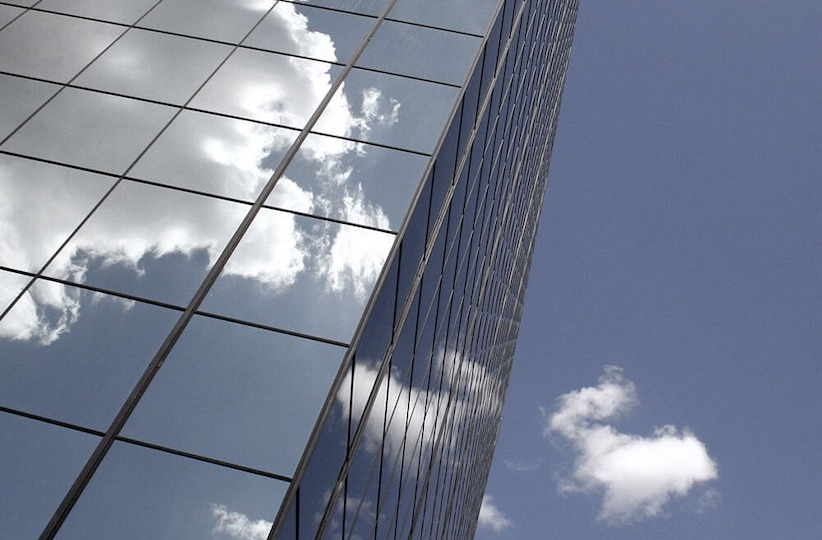 corner of a glass building with a reflection of clouds
