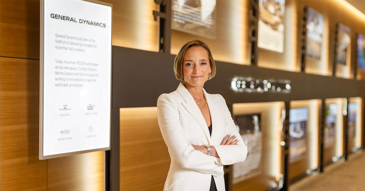 Amy Gilliland by GD history timeline wall at GDIT HQ