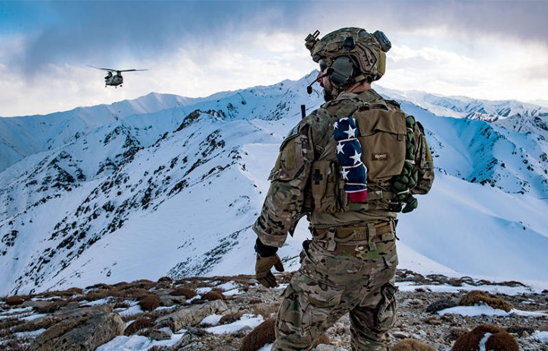 soldier standing over snowy mountains, helicopter seen afar 
