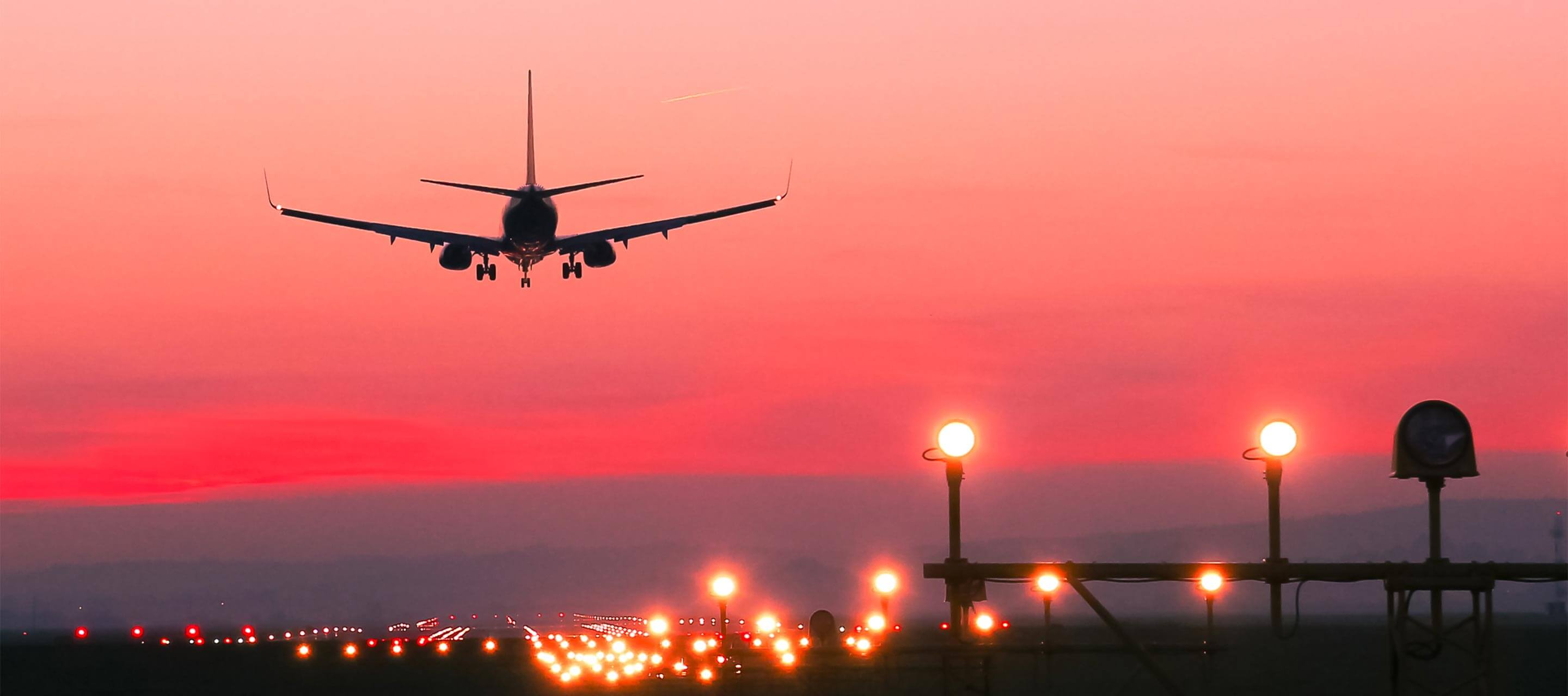 image of a plane taking off the runway at sunset with a bright pink/red sky