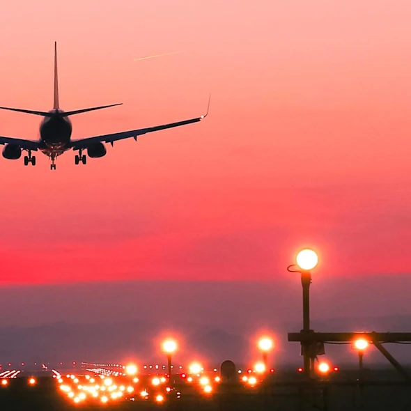 image of a plane taking off the runway at sunset with a bright pink/red sky