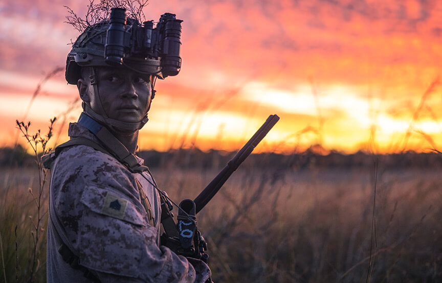 soldier in camo looking away, sunset behind him