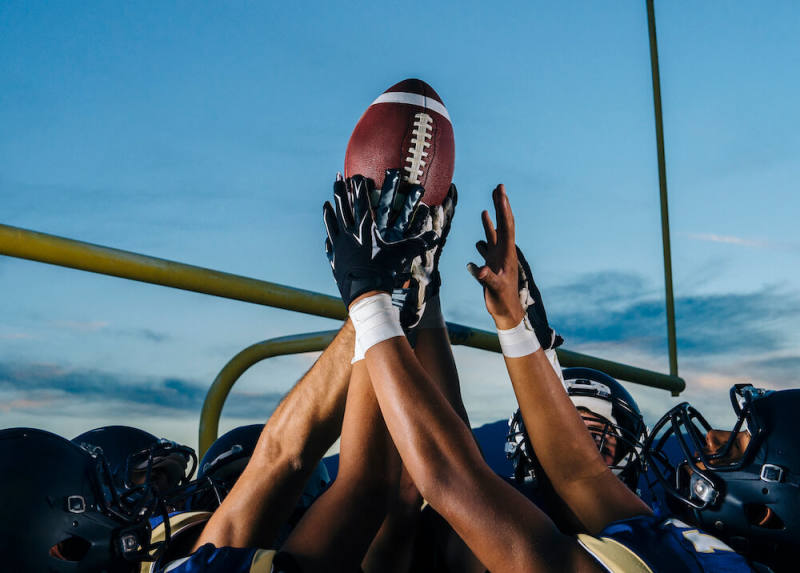 group of football player's hands holding up a football