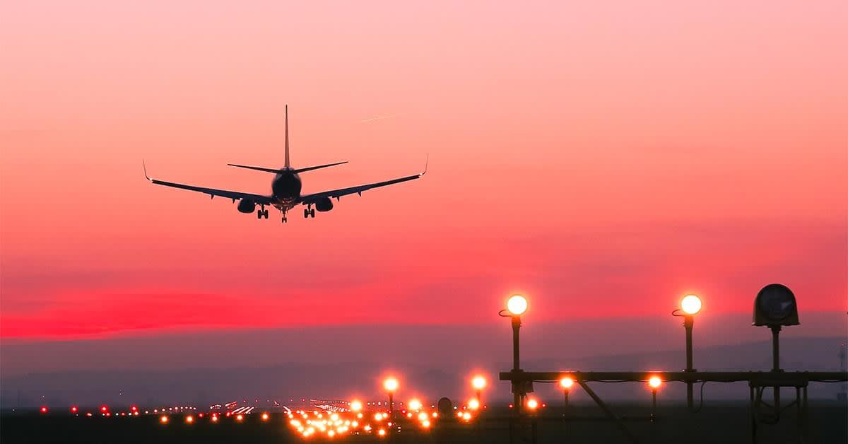image of a plane taking off the runway at sunset with a bright pink/red sky