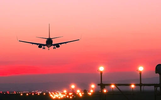 image of a plane taking off the runway at sunset with a bright pink/red sky