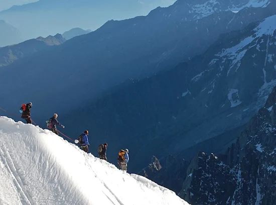 image of a group of hikers going down a snowy hill, mountains in background