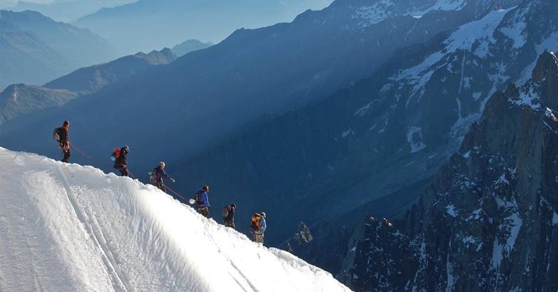 image of a group of hikers going down a snowy hill, mountains in background