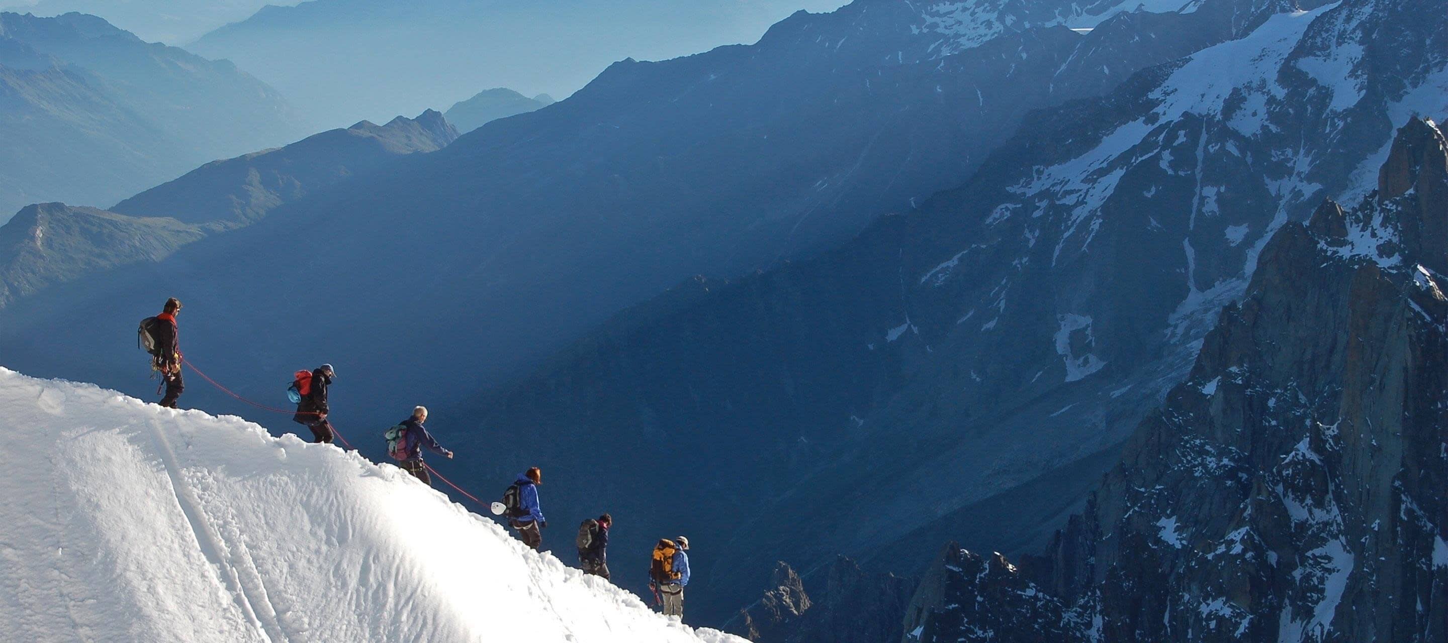 image of a group of hikers going down a snowy hill, mountains in background
