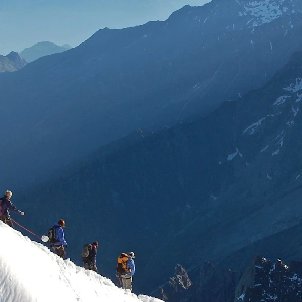 image of a group of hikers going down a snowy hill, mountains in background