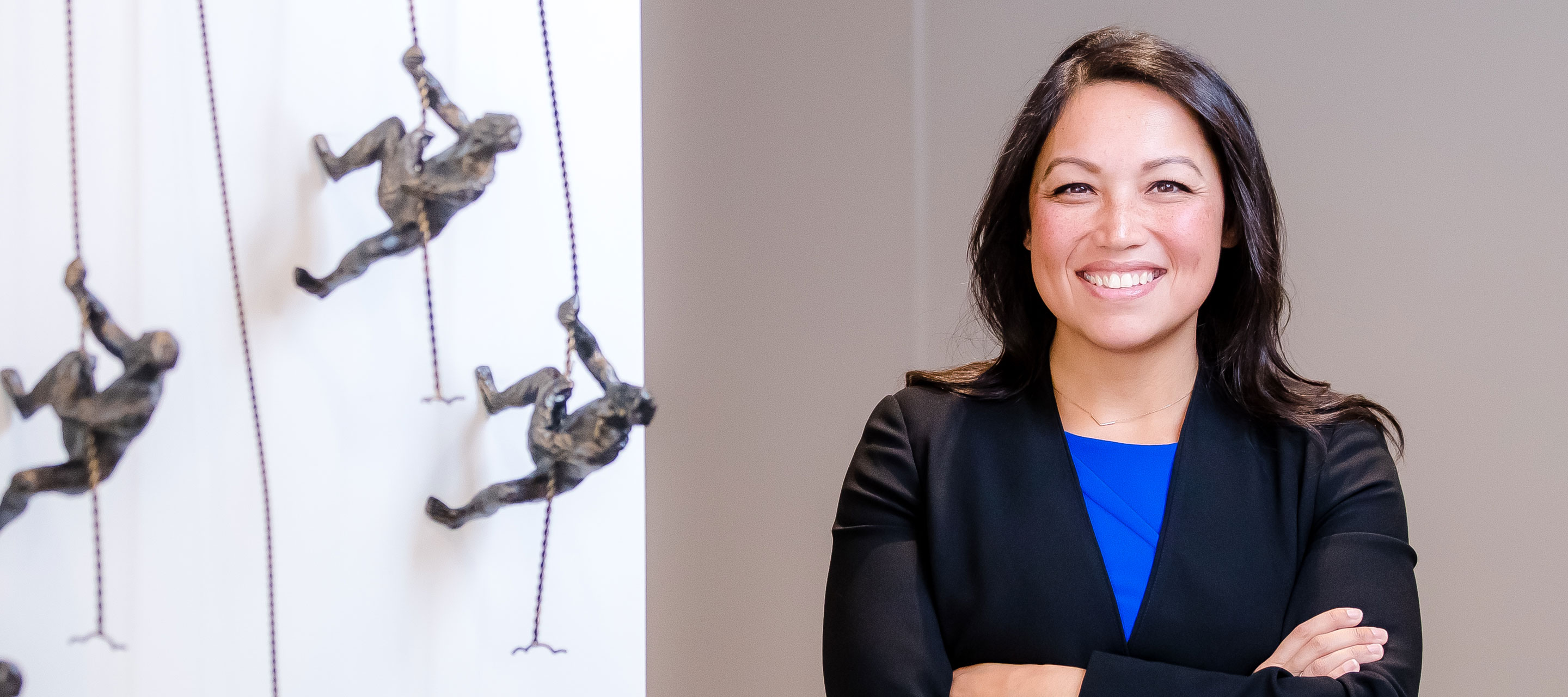 GDIT's Joleen S with arms crossed next to figurines of soldiers climbing wall 